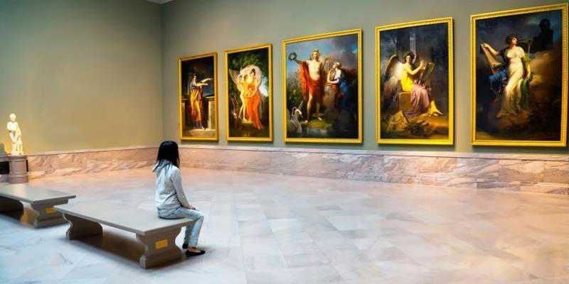 Une visiteuse assise contemple plusieurs tableaux dans une galerie