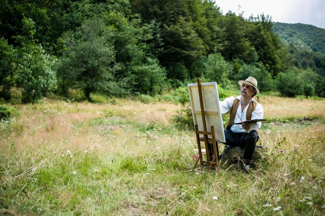 Artiste peignant en plein air, face à une forêt et une prairie