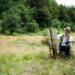 Artiste peignant en plein air, face à une forêt et une prairie